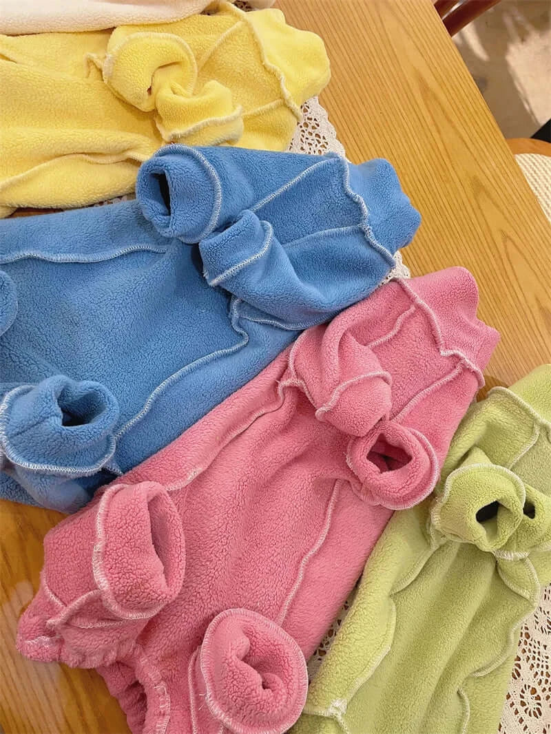 Colorful fleece coats for Sphynx cats in pink, blue, green, and yellow displayed on a wooden table.