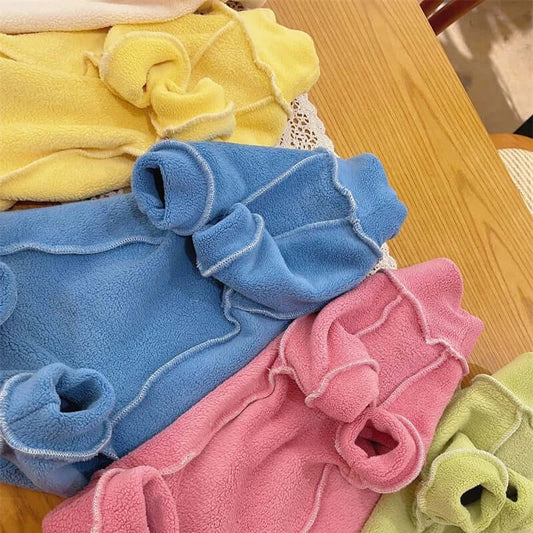 Colorful fleece coats for Sphynx cats in yellow, blue, pink, and green laid on a wooden table.